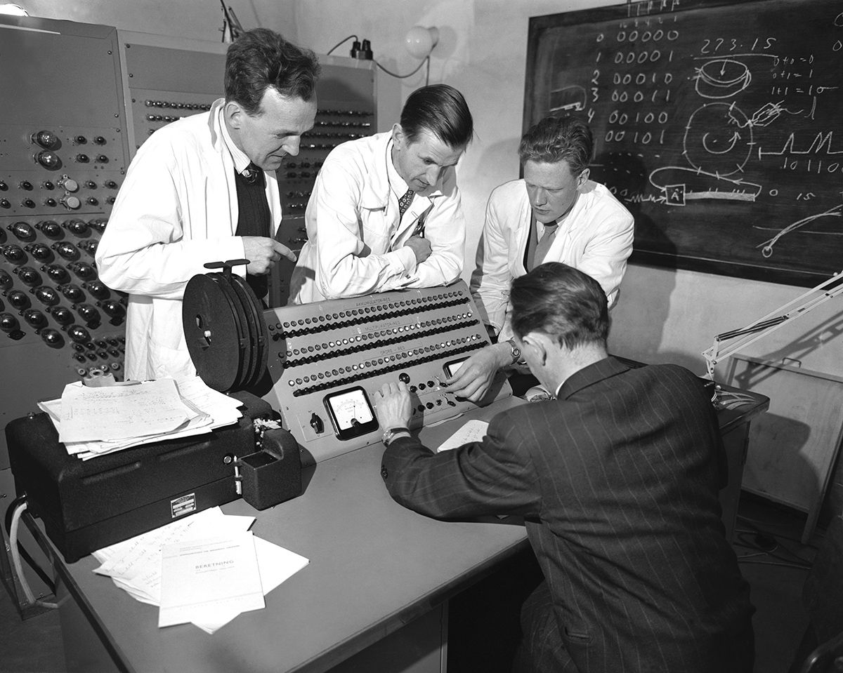 Fotografi som viser fire menn rundt en datamaskin