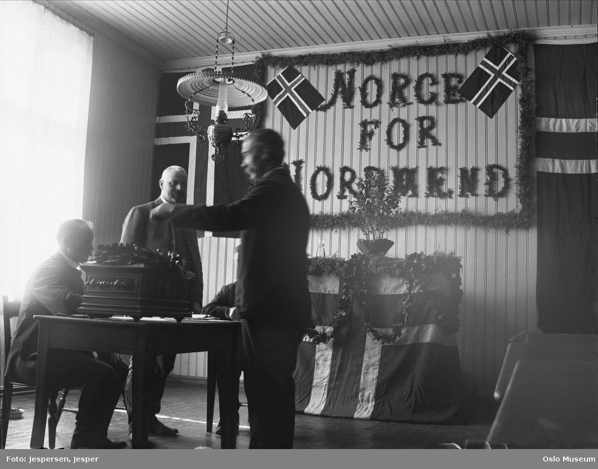 Foto av stående mann som gir stemmeseddel til mann sittende bak et bord