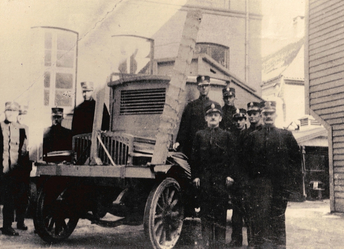 9 politimenn i uniform oppstilt ved siden av en pansret bil