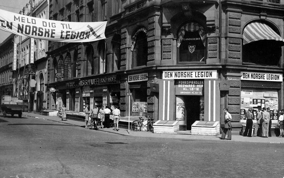Gate med folk som går og sykler. En plakat: "Meld dig til den norske legion" går over veien.