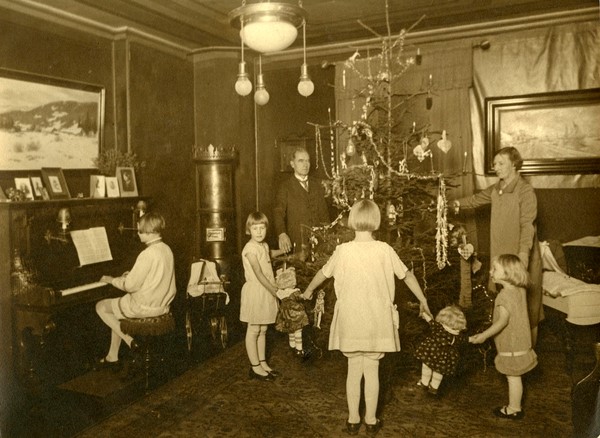 Fotografi av familie som går rundt juletre. Jente spiller piano