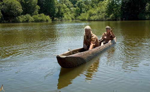 Fotografi av to personer i stokkebåt, steinalderkostymer