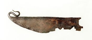 Denne barberkniven av bronse ble funnet ved Velo Vestre på Hadeland, og er formet som en båt og dekorert med båtmotiv. Legg merke til de utsmykkede stevnene. Les mer om hva båten symboliserte i bronsealderen . Foto: Ove Holst/Kul­tur­his­torisk Mu­seum, UiO/ CC BY-SA 4.0