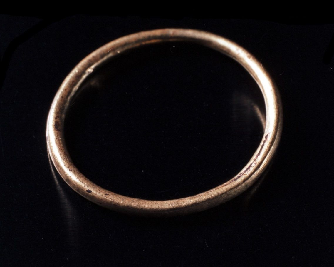 Foto. Svart bakgrunn. Helt enkel sirkelformet ring i gull som motiv. Gullringen er lyssatt og eksponert slik at framre del kjem i fokus, medan bakredel av ringen er litt dus.
