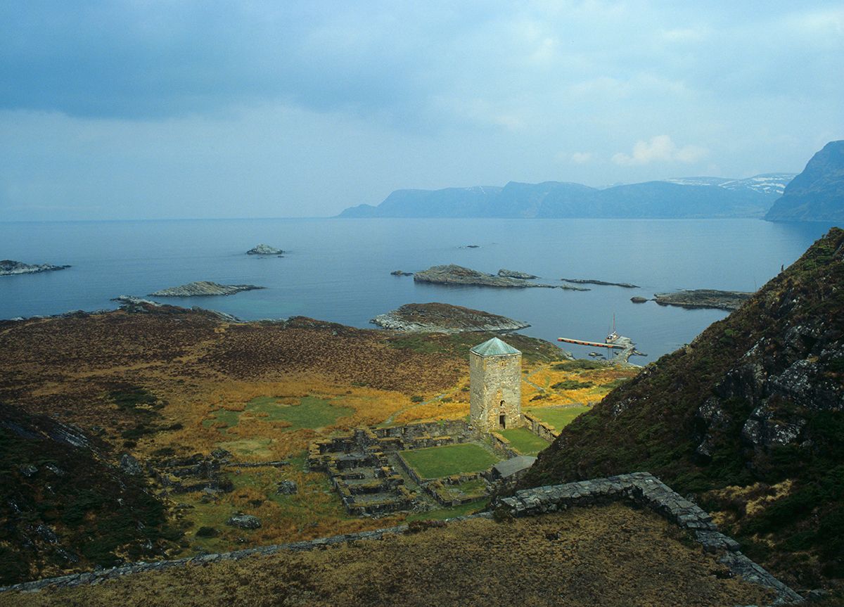 Fotografi fra fjellside med utsikt ned mot klosterruiner, hav i bakgrunn