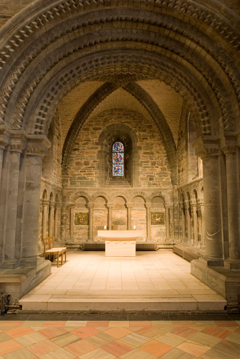 Bildet viser kapell i Nidarosdomen. Høye gotiske buer bærer taket, mens romanske buer er hogget i relieff i veggen. I bakre vegg et slankt glassmaleri