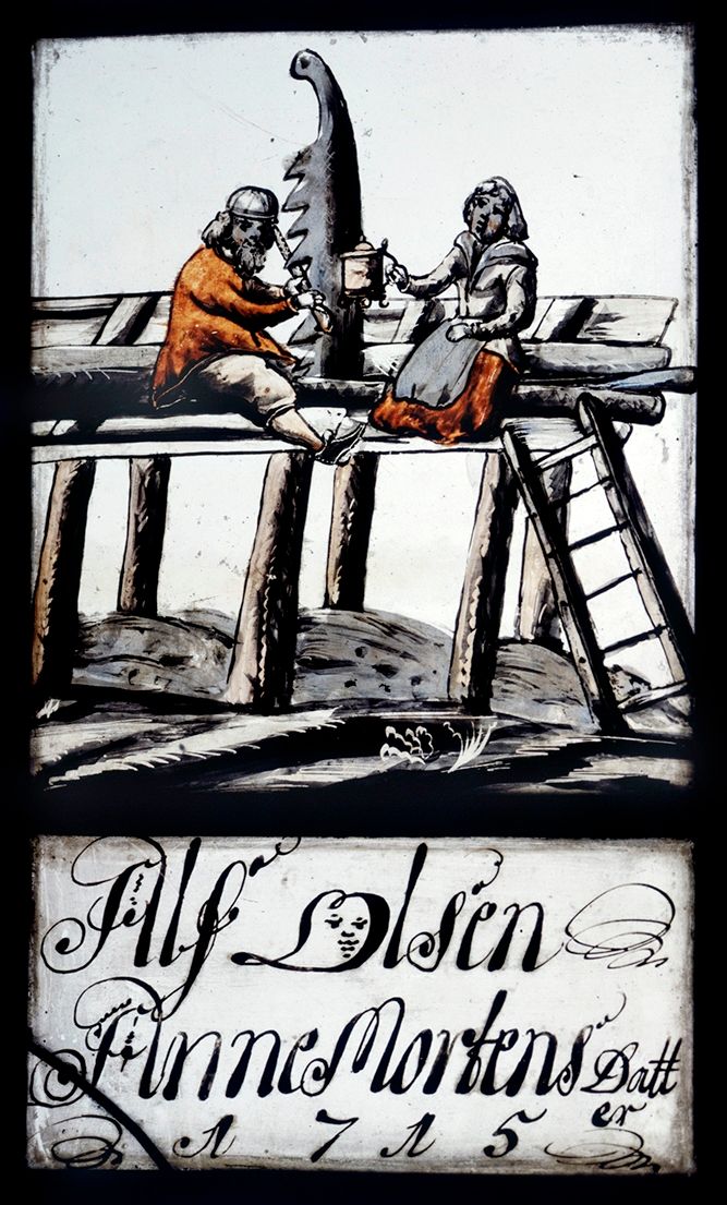 glassmaleri med påskrift: "Alf Olsen, Anne Mortensdatter, 1715". Mann sitter og filer sagblad, kvinne tilbyr et krus