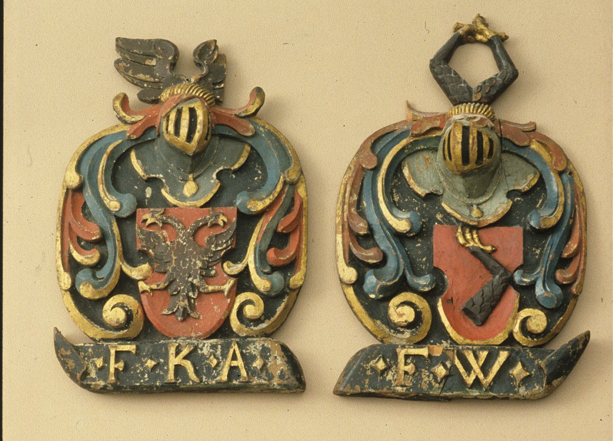 Fotografi av to gipsavstøpninger i farger, som viser våpenskjold. Til venstre initialene "F.K.A." med en tohodet fugl i motivet, og til høyre initialene "F.W." med et fuglebein i motivet