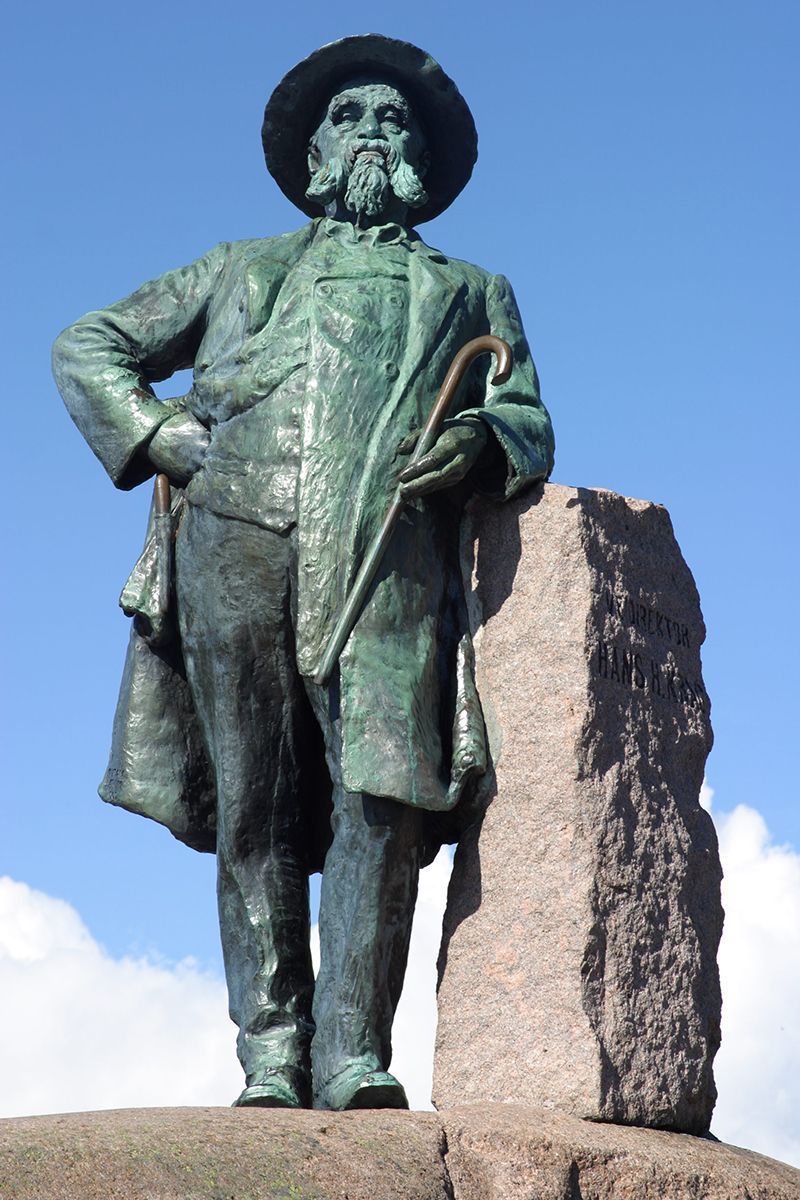 Fotografi av statue av mann med hatt, skuende blikk. Mot blå himmel