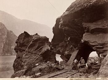Jernbanekonstruksjon i fjordlandskap bød på mange utfordringer: Her har en steinblokk løsnet fra fjellsiden. Vossebanen ble bygd mellom 1875 og 1883. Les mer om hvordan Norge ble bundet tettere sammen i løpet av siste halvdel av 1800-tallet . Foto: Axel Lindahl/Nasjonalbiblioteket/ CC PDM