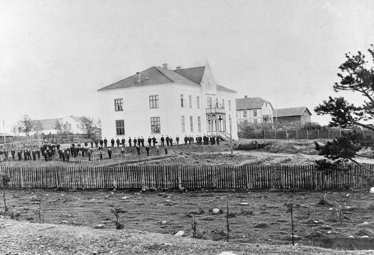 Fotografi av bygning, mennesker i forgrunn. Hamar stiftseminarium