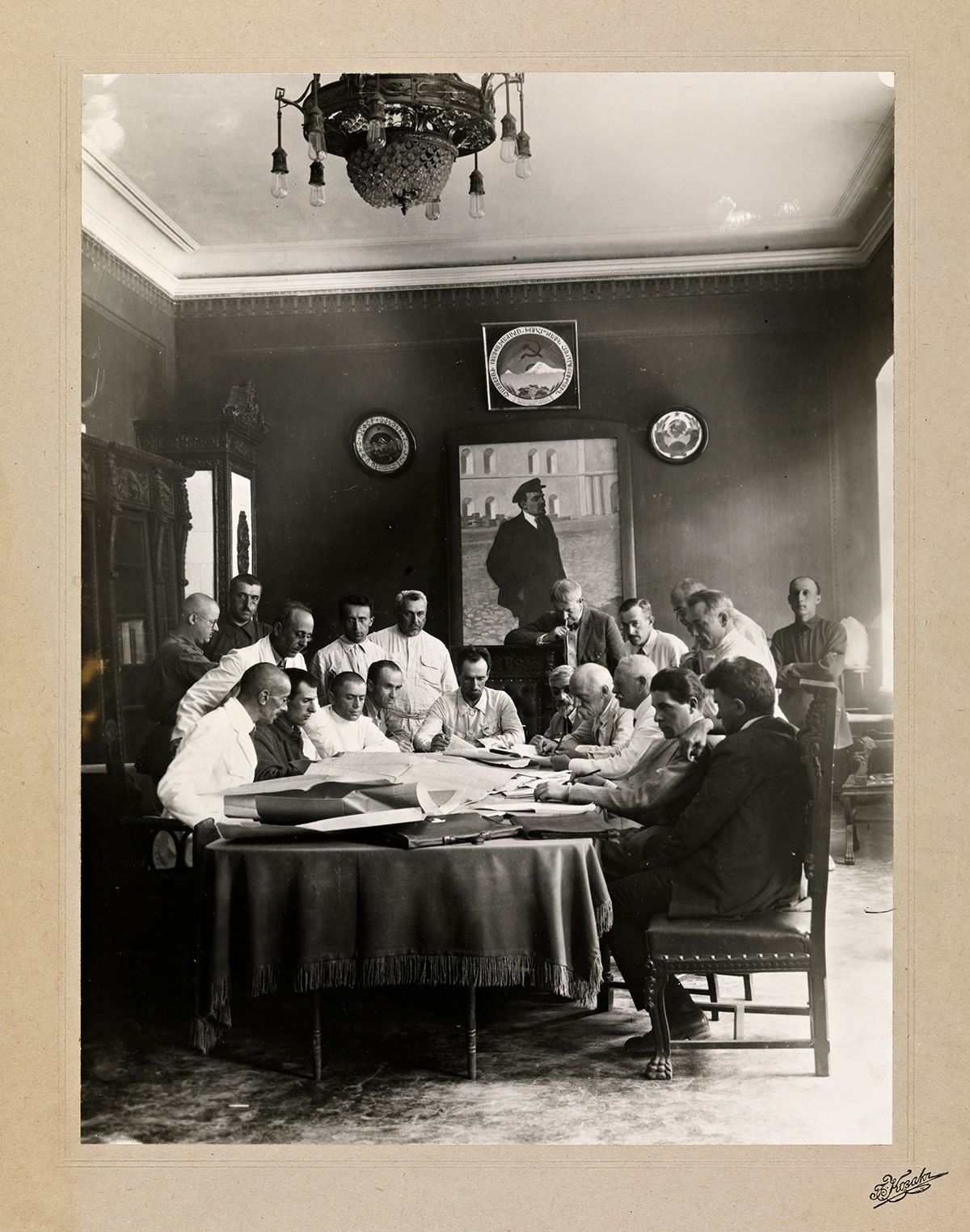 Fotografi av Armeniakommisjonen, sittende rundt et bord, disktuterer. Portrett av Lenin i bakgrunn