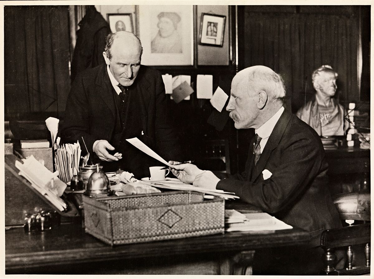 Fotografi av Fridtjof Nansen sittende ved et skrivebord, overrekker et papir til John Lewis Paton
