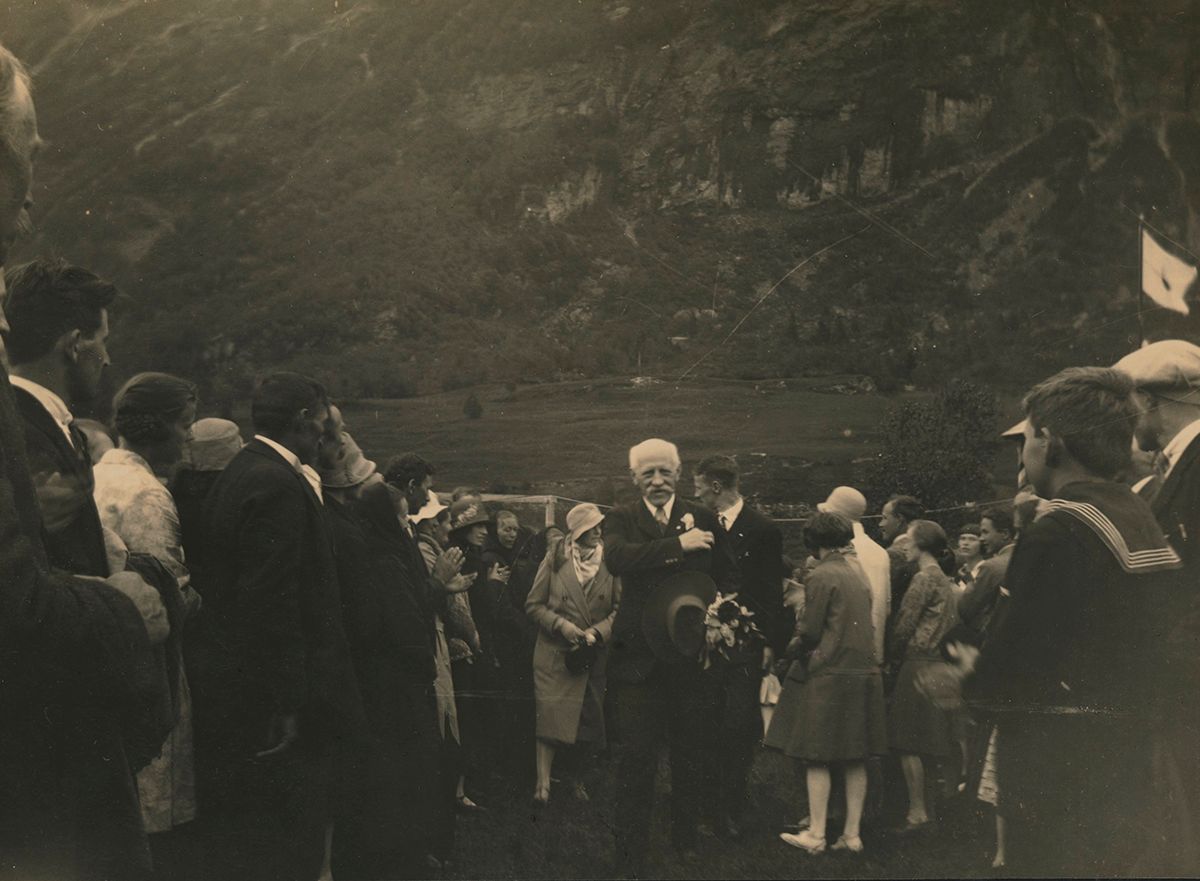 Fotografi av Fridtjof Nansen gående i oppoverbakke og blir mottatt av folkemengde