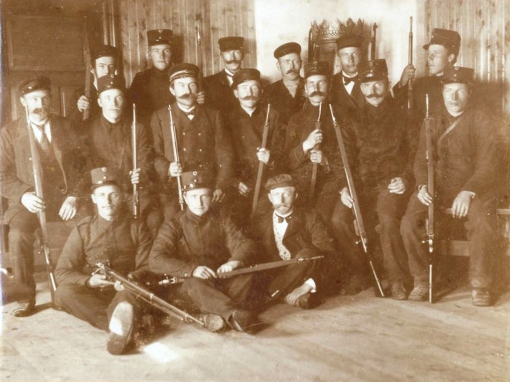 Fotografi av oppstilte menn i uniform (noen uten), alle med Krag-Jørgensen-rifler