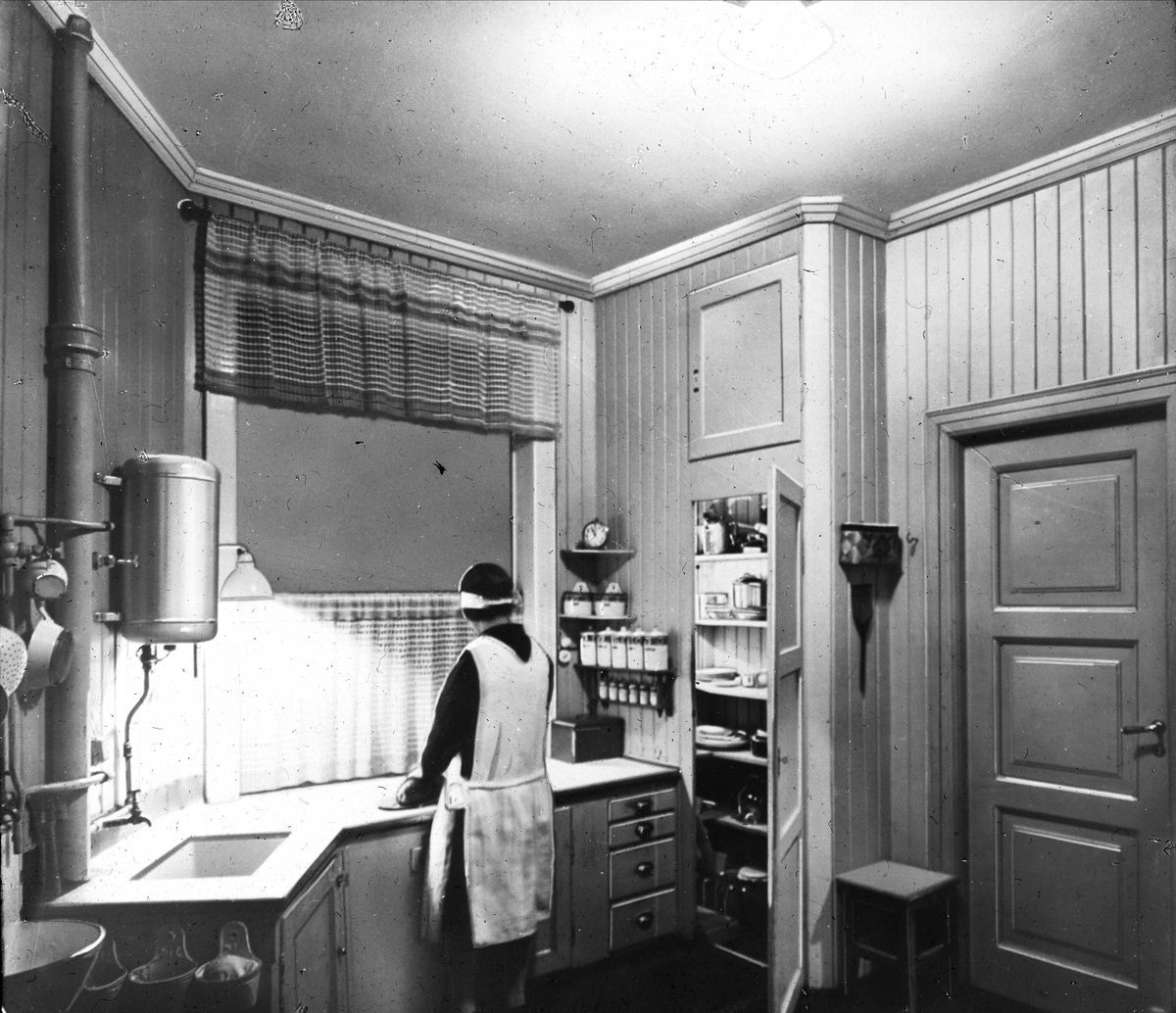 Fotografi av kvinne med ryggen til kamera, arbeider på kjøkkenbenk ved hjelp av elektrisk lys.