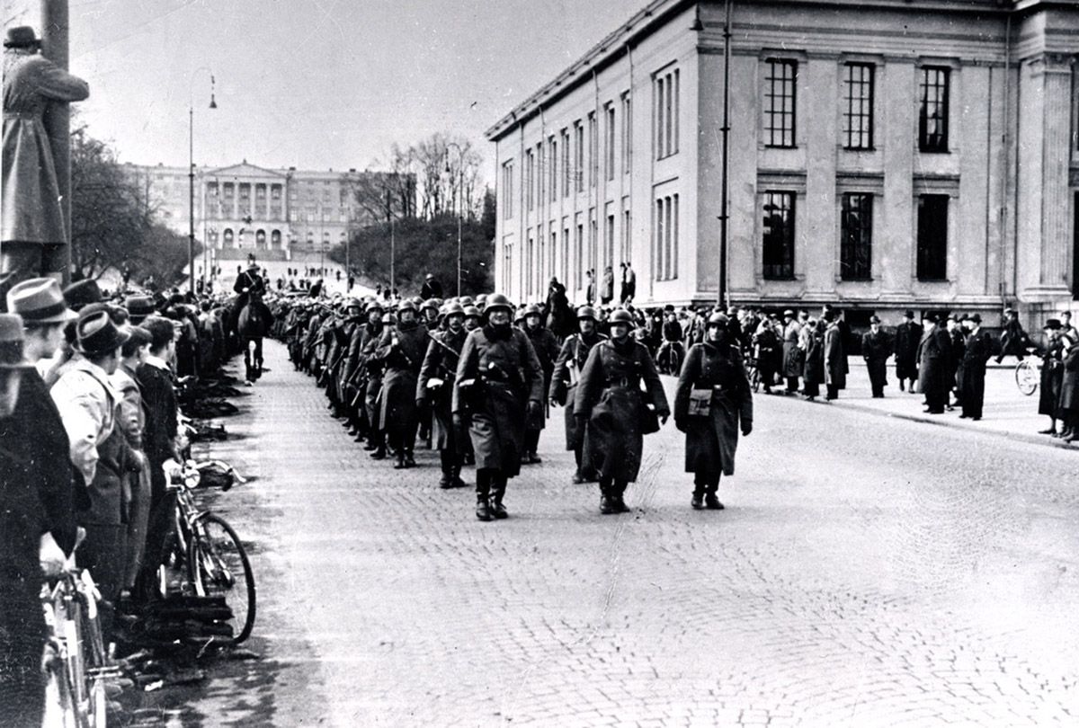 Oslo, Karl Johans gate. Det kongelige slott i bakgrunnen. Tyske tropper marsjerende nedover i retning Oslo sentralstsjon. Folkemengde ser på de marsjerende soldatene.
