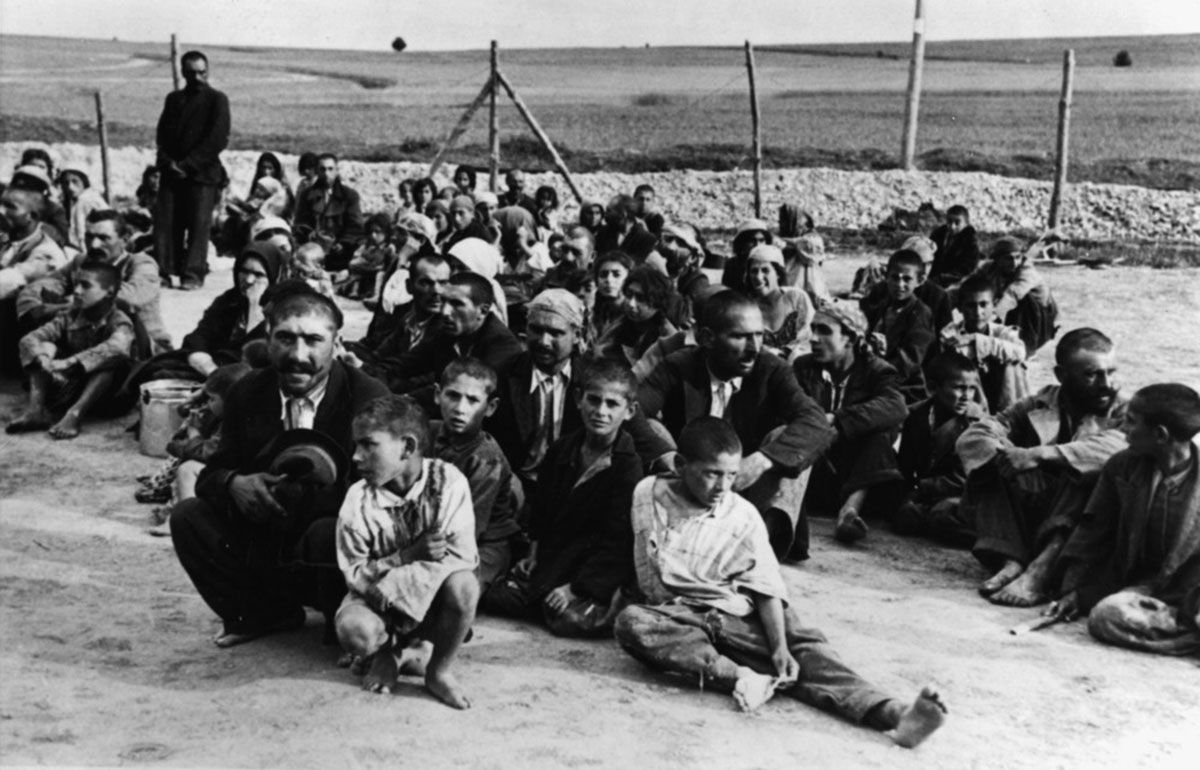 Fotografi, tatere/romanifolk sittende på bakken, i konsentrasjonsleir