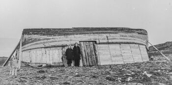 Da innbyggerne i Finnmark og Nord-Troms fikk ordre om å evakuere i påvente av tyskernes bruk av brent jords taktikk , valgte 23 000 å trosse ordren og ble værende i den ødelagte landsdelen. En rekke provosoriske hjem ble bygd av de materialer som den gjenverende befolkningen kom over. Her er en sjekte blitt til tak i et midlertidig hjem for åtte personer, to kyr og en geit i Gamvik. Denne typen byggverk fantes det flere av og de ble etter hvert dekket til med torv og jord for å holde vind og kulde ute. Foto: Ole Friele Backer/Riksarkivet, PA-1209 NTBs krigsarkiv/ CC BY-SA