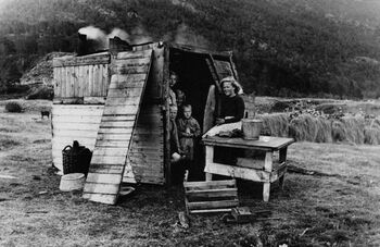 Store deler av befolkningen som hadde blitt tvangsevakuert fra Finnmark og Nord-Troms i 1944, vendte tilbake til landsdelen til tross for hjemreiseforbud fra myndighetene. Mens gjenreisningen pågikk måtte mange av dem bo under svært kummerlige forhold i provisoriske hjem . Her ser det midlertidige hjemmet til en familie i Kvænangen i Nord-Troms i 1945. Foto: J. Utheim/Norsk Teknisk Museum