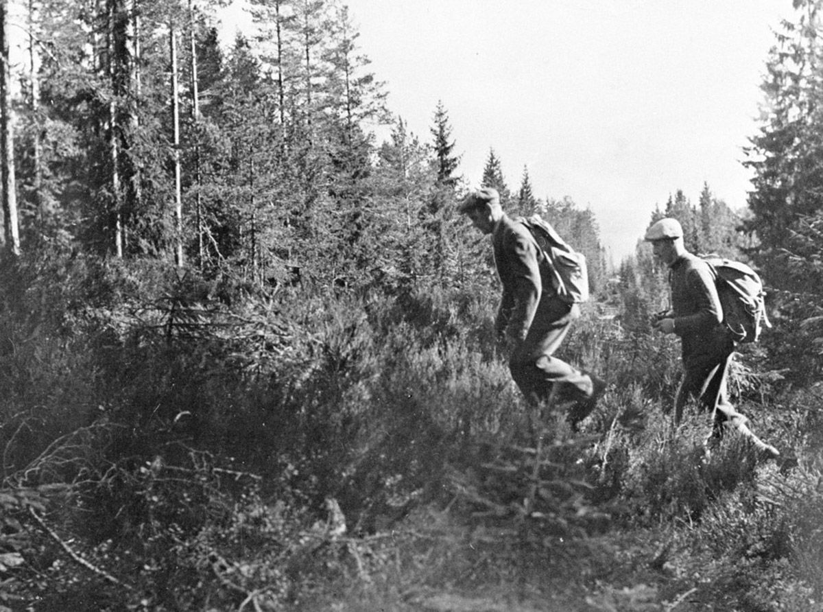 Fotografi av to menn som krysser langstrakt rydning i skog: grensen til Sverige