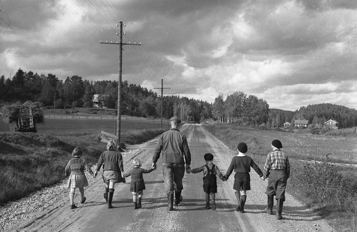 Fotografi, mann med tre barn i hver arm, leiende på rekke langs landevei