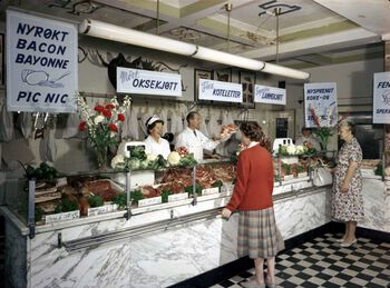 Etter at rasjonering på kjøtt ble opphevet i 1952, kunne forretningene igjen fritt selge slaktevarer. Her tilbyr Johs. Linde kolonialforretning i Bentsegata 2 på Sagene i Oslo blant anna på «nyrøkt bacon, bayonne, pic nic» og «nysprengt koke- og stekeflesk». Bilde tatt i 1961. Les mer om økt levestandard og sosialdemokratisk forbrukskultur . Foto: Atelier Rude/Byhistorisk samling/Oslo museum/ CC BY-SA