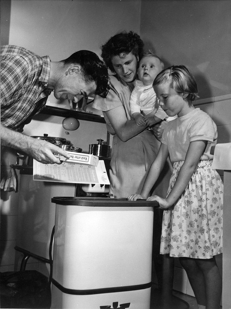 Fotografi av familie rundt vaskemaskin. Mannen leser bruksanvisning