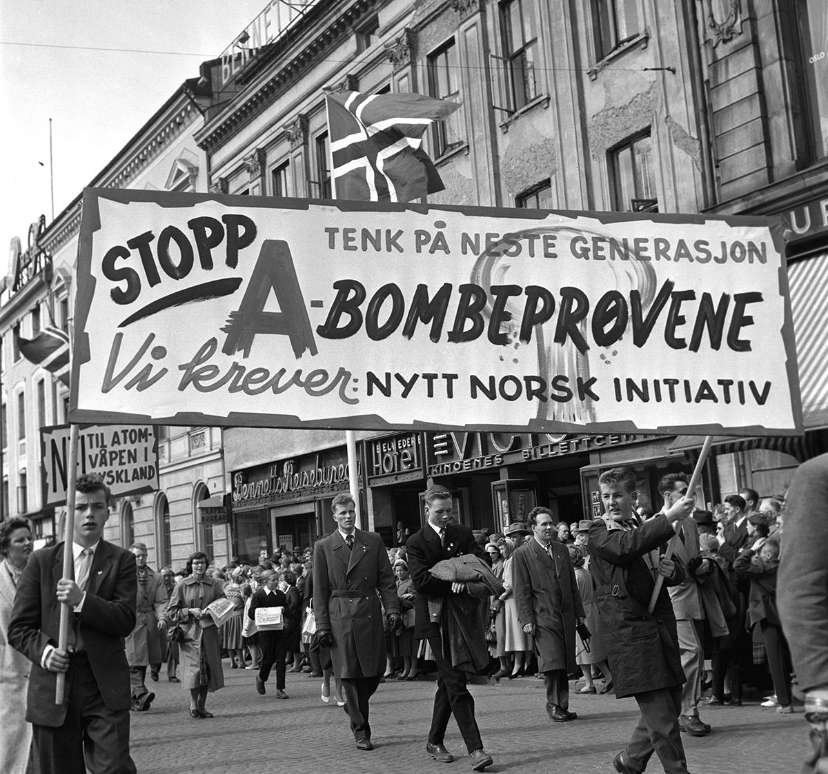 Fotografi av demonstrasjonstog på Karl Johan: parole med tekst: "Stopp A-bombeprøvene. Tenk på neste generasjon. Vi krever nytt norsk initiativ"