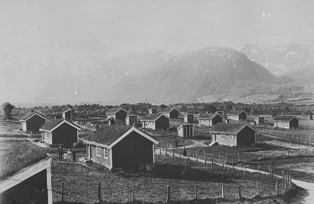 Fotografi som viser Svanviken arbeidskoloni: mange små hytter i landskap, høye fjell i bakgrunn