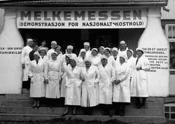 Å få Norges befolkning til å drikke mer melk var et politisk satsningsområde i mellomkrigstiden . Et virkemiddel for å spre informasjon om melkens gode egenskaper var Melkemessen. På messen ble det holdt foredrag og demonstrasjoner som alle hadde som mål å få husmoren til å handle inn og bruke mer melk. Messen varte i en ukes tid og skapte liv og røre på små og store steder i landet. Her ser vi dekorasjonen av inngangspartiet da messen ble holdt på Folkets hus i Moelv i 1934. Foto: Mikkel Sveinhaug/Domkirkeodden/ CC BY