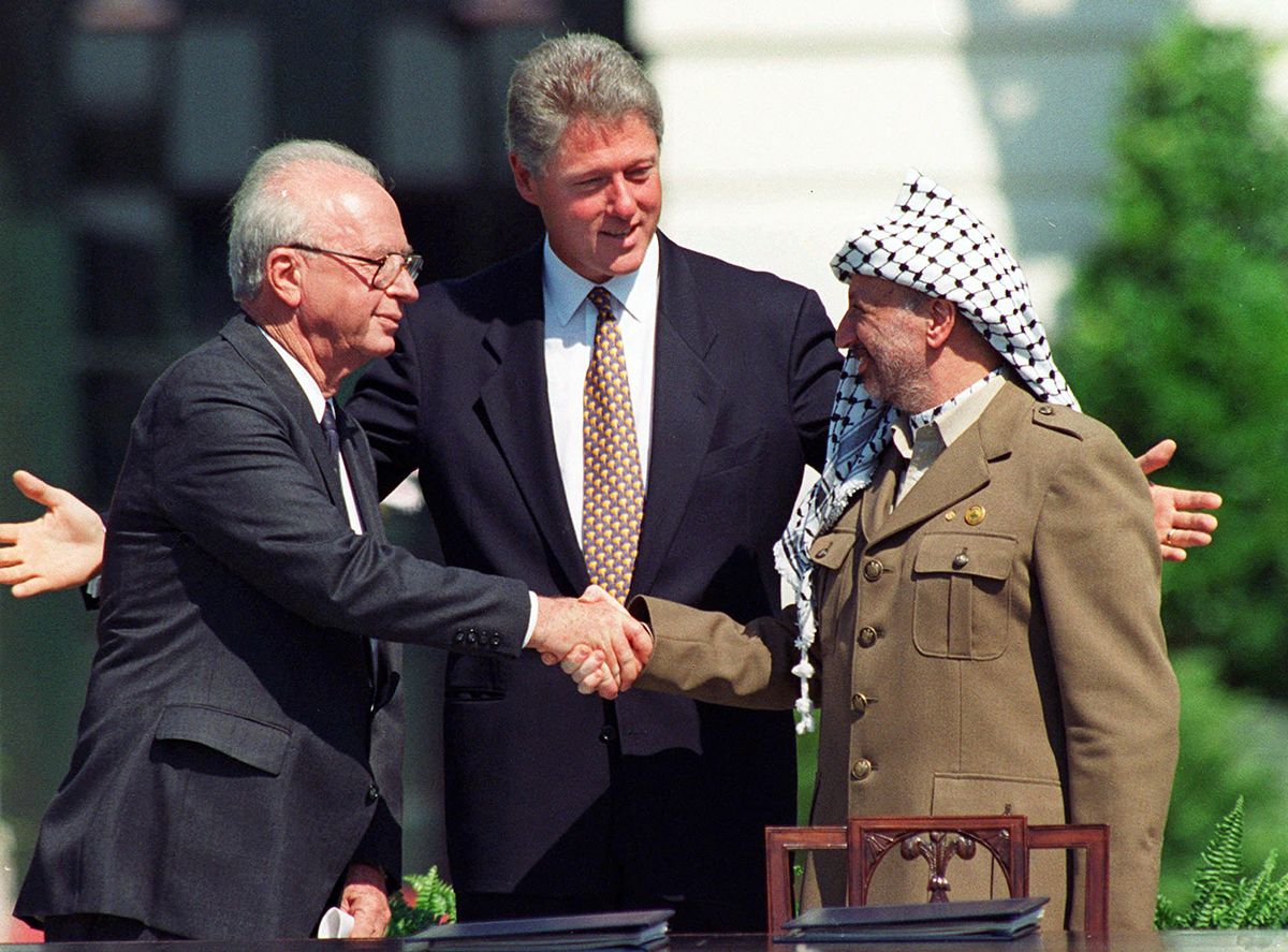 Fotografi som viser Yitzhak Rabin til venstre og Yassir Arafat til høyre, håndtrykk. I midten står Bill Clinton og smiler, utstrakte armer