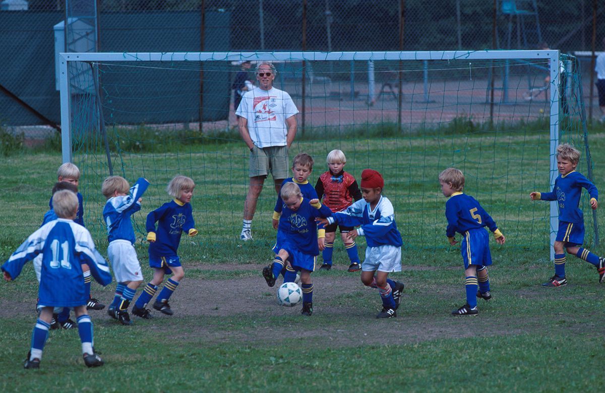 Fotografi som viser små gutter som spiller fotballkamp. En gutt med rød turban