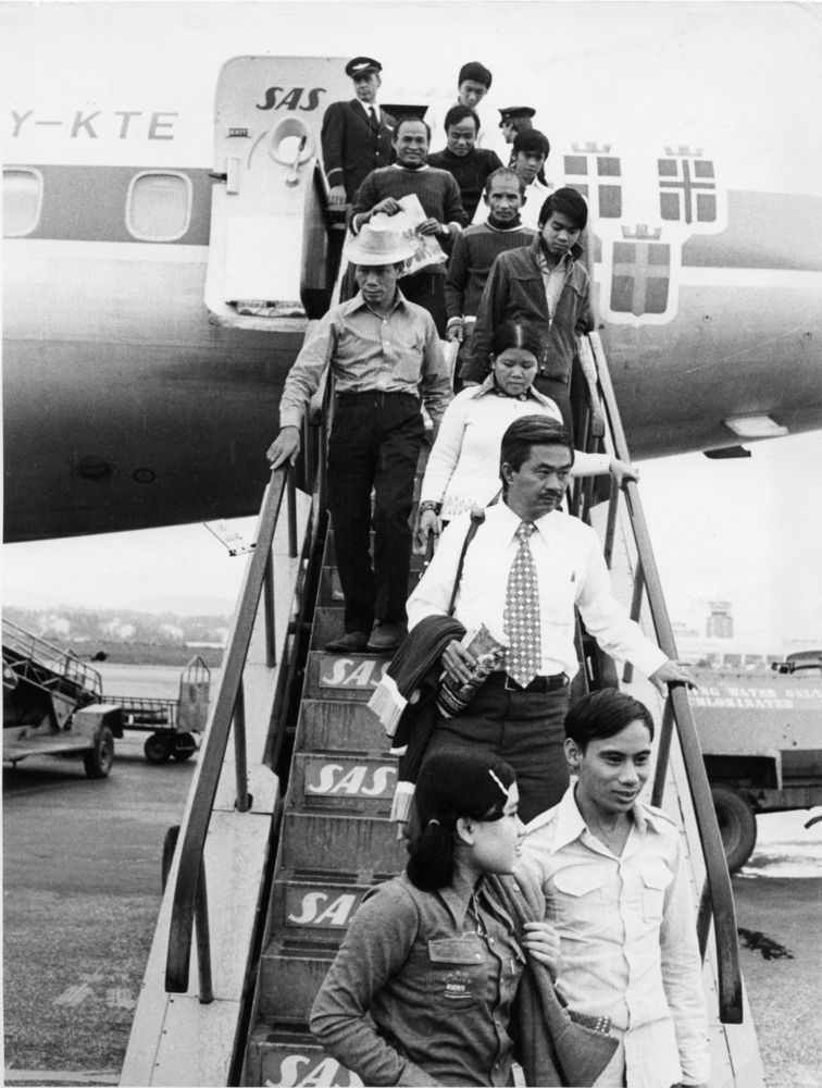 Svart-hvitt foto av pent kledde flyktninger fra Vietnam som stiger ned fra SAS-fly.
