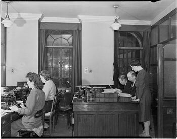 Nortraship (The Norwegian Shipping and Trade Mission) administrerte den norske handelsflåten under krigen. Bildet er fra Nortraship kontorer i London, den maritime avdeling, hvor&amp;#160;Mrs. Holmsen, Miss Knudtzon, Harald Nicolaisen, J. Mathiesen, Miss Salmon jobber.
